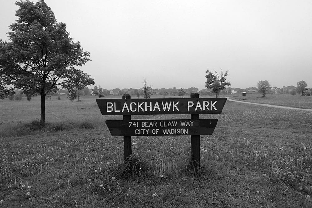 Image of park sign reading "Blackhawk Park" in a mundane landscape