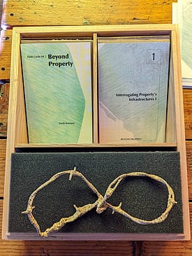 Wooden box in three sections with a green and yellow colored book, pink and blue cards, and a paper-cover barbed wire