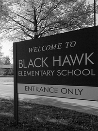 Black and white photo of sign reading: Welcome to Black Hawk Elementary School - Entrance Only with trees in the background