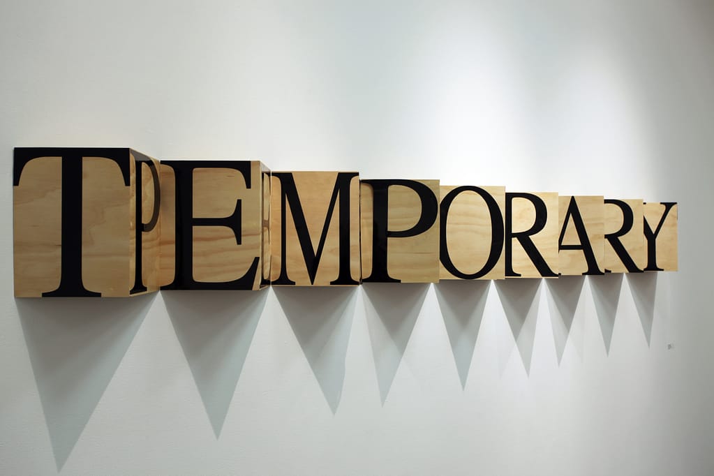 Wooden boxes protrude at an angle from the wall with vinyl letters reading "temporary"