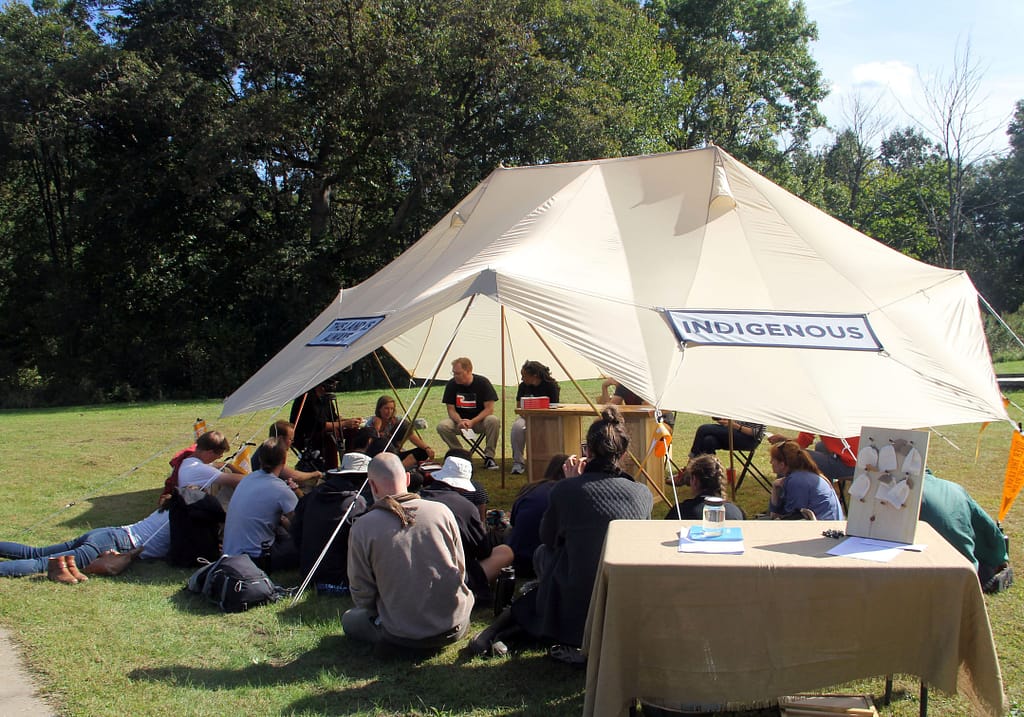 A crowd of people gather outdoors beneath oopen-sided tent