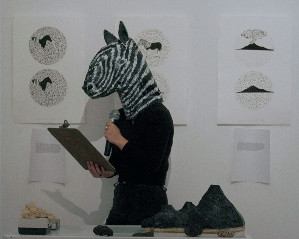 A performer reading from a clipboard wearing a papier mache a zebra head