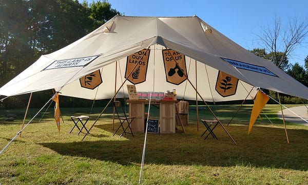 Open-sided tent with banners and a wooden tablee