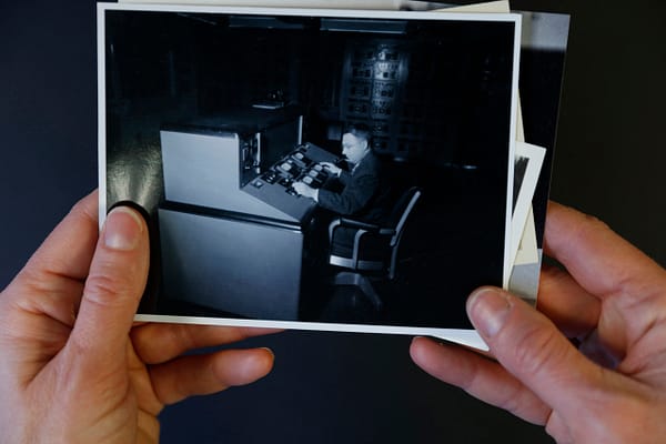Video still showing hands holding image of artist's grandfather at a control console.